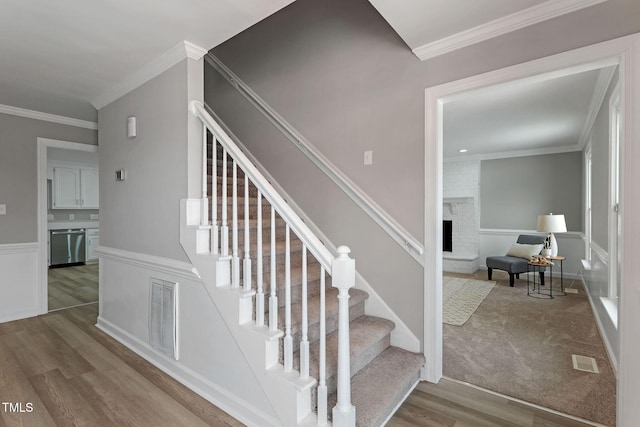 stairs with crown molding, a brick fireplace, and hardwood / wood-style floors