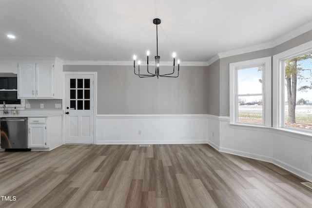 unfurnished dining area featuring an inviting chandelier, ornamental molding, sink, and light hardwood / wood-style floors