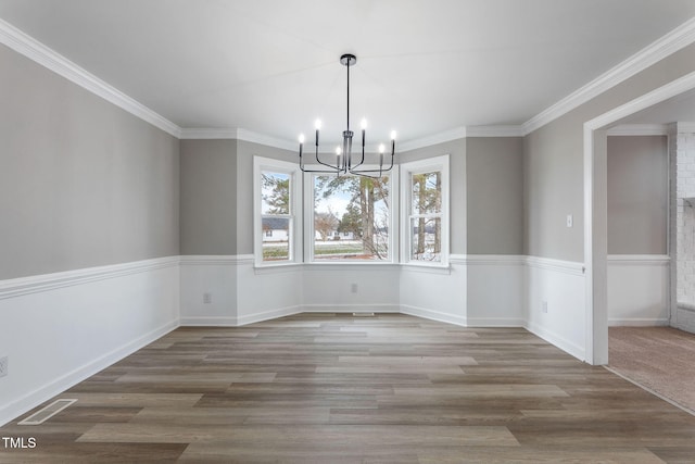 unfurnished dining area with an inviting chandelier, wood-type flooring, and ornamental molding