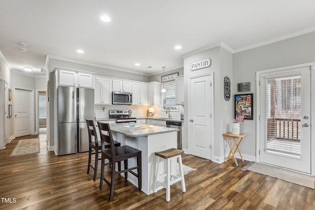 kitchen featuring a breakfast bar, appliances with stainless steel finishes, white cabinets, a kitchen island, and decorative light fixtures