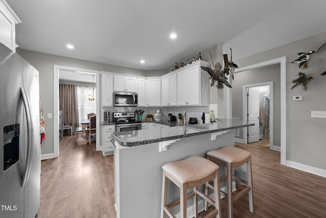 kitchen with appliances with stainless steel finishes, white cabinetry, dark stone countertops, a kitchen breakfast bar, and kitchen peninsula