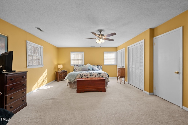 carpeted bedroom featuring ceiling fan, two closets, and a textured ceiling