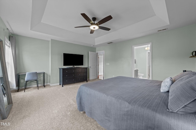 bedroom with light carpet, connected bathroom, a raised ceiling, and ceiling fan