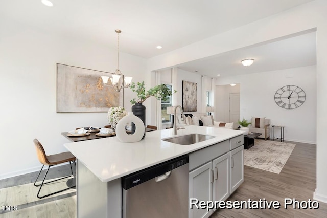 kitchen featuring light hardwood / wood-style flooring, decorative light fixtures, sink, stainless steel dishwasher, and a center island with sink