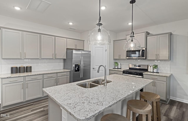 kitchen featuring sink, stainless steel appliances, hanging light fixtures, and a center island with sink