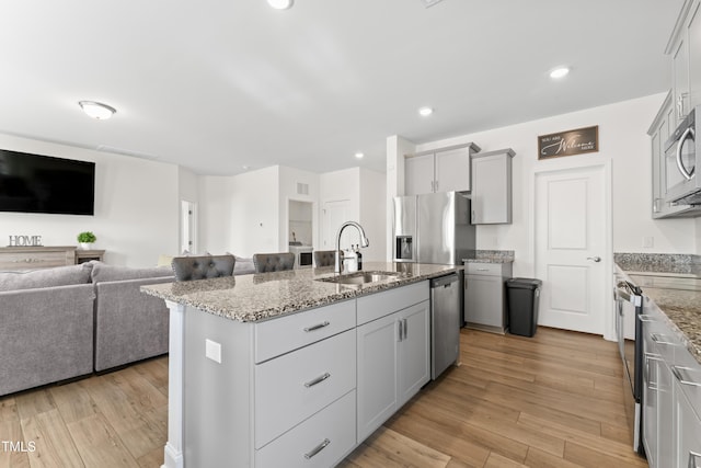 kitchen featuring sink, gray cabinetry, light hardwood / wood-style flooring, appliances with stainless steel finishes, and an island with sink