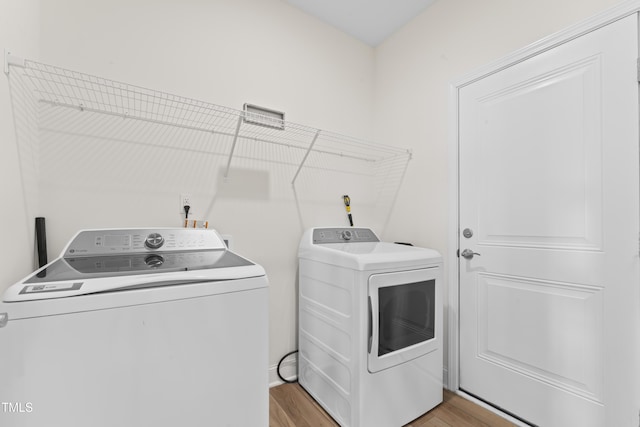 clothes washing area with washing machine and dryer and light wood-type flooring