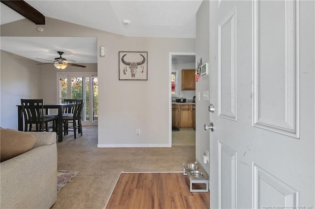 foyer entrance featuring ceiling fan, light colored carpet, and vaulted ceiling with beams