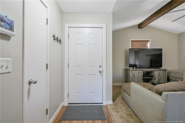 foyer featuring light wood-type flooring, a textured ceiling, and vaulted ceiling with beams