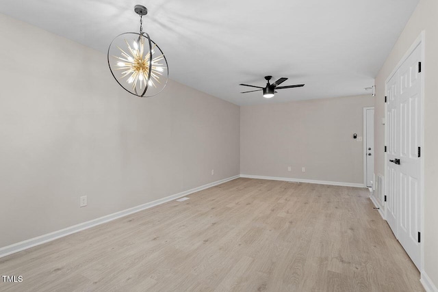 spare room featuring light wood-type flooring and ceiling fan with notable chandelier