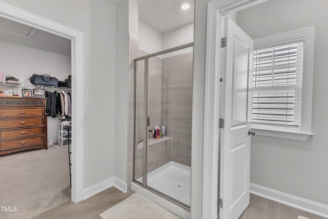 bathroom with a spacious closet, a stall shower, and baseboards