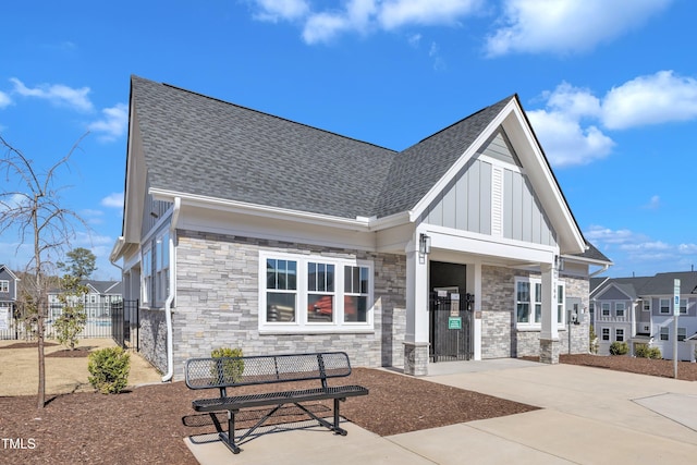 view of front of home featuring stone siding, fence, a residential view, roof with shingles, and board and batten siding