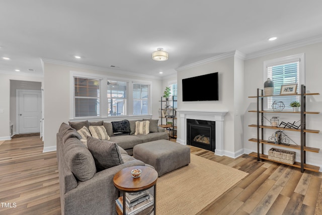 living room with baseboards, recessed lighting, light wood-style floors, a glass covered fireplace, and crown molding