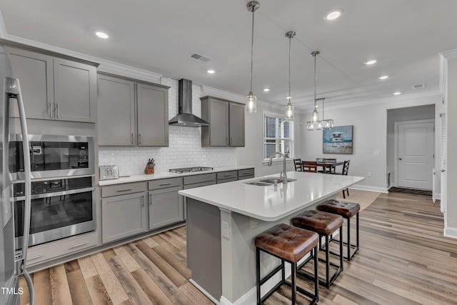 kitchen featuring ornamental molding, gray cabinets, a sink, stainless steel appliances, and wall chimney exhaust hood