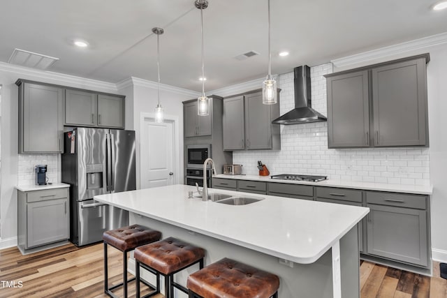 kitchen featuring wall chimney range hood, gray cabinetry, appliances with stainless steel finishes, and a sink