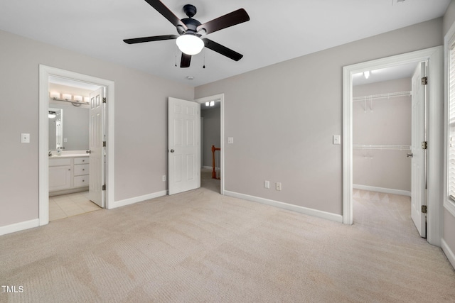 unfurnished bedroom with a spacious closet, ensuite bath, a closet, ceiling fan, and light colored carpet