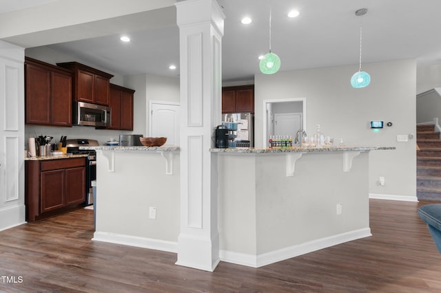 kitchen featuring hanging light fixtures, light stone countertops, a kitchen bar, dark hardwood / wood-style floors, and stainless steel appliances