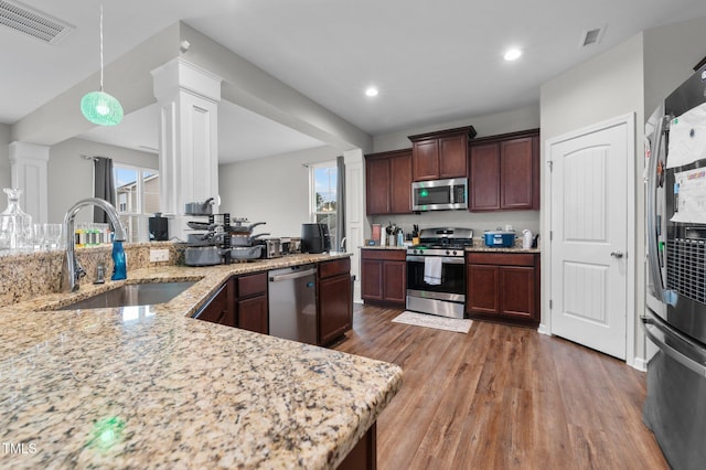 kitchen featuring appliances with stainless steel finishes, wood-type flooring, hanging light fixtures, sink, and light stone counters