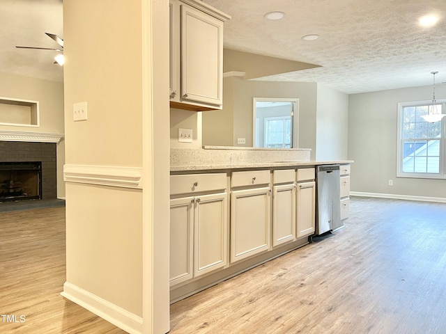 kitchen featuring light stone countertops, pendant lighting, light hardwood / wood-style floors, a brick fireplace, and stainless steel dishwasher