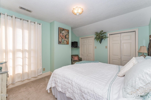 carpeted bedroom featuring visible vents, vaulted ceiling, and a textured ceiling