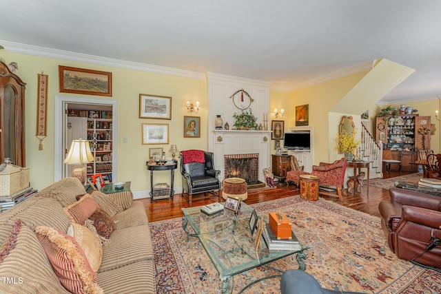 living area with baseboards, a large fireplace, stairway, crown molding, and wood finished floors