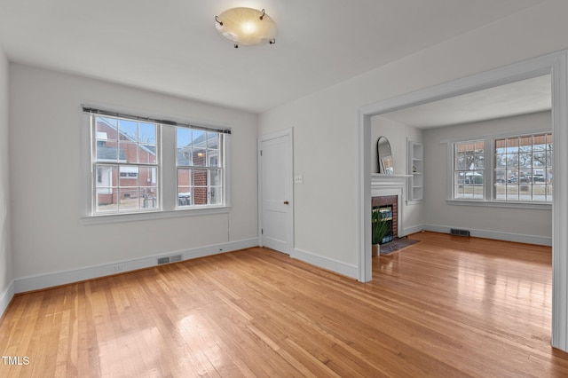 unfurnished living room featuring a fireplace, built in features, and light wood-type flooring