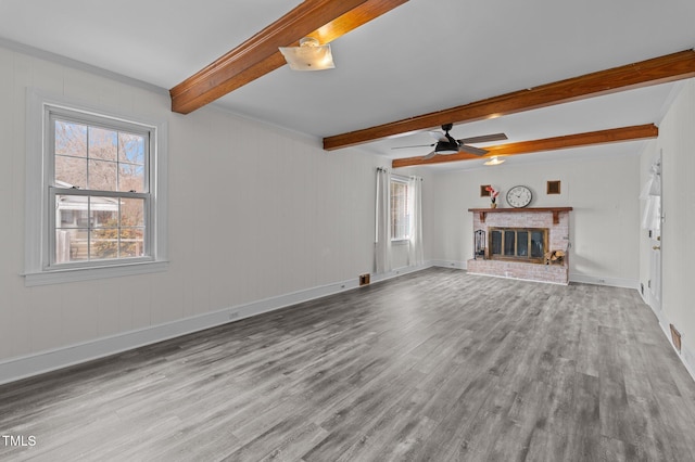 unfurnished living room featuring a healthy amount of sunlight, a fireplace, light hardwood / wood-style floors, and beamed ceiling