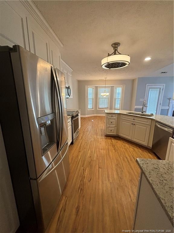 kitchen with hanging light fixtures, sink, white cabinetry, light hardwood / wood-style floors, and stainless steel appliances