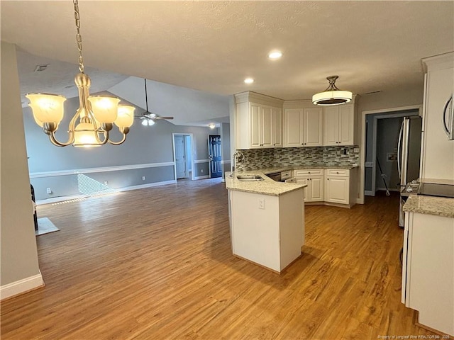 kitchen with light stone countertops, white cabinets, tasteful backsplash, hanging light fixtures, and kitchen peninsula