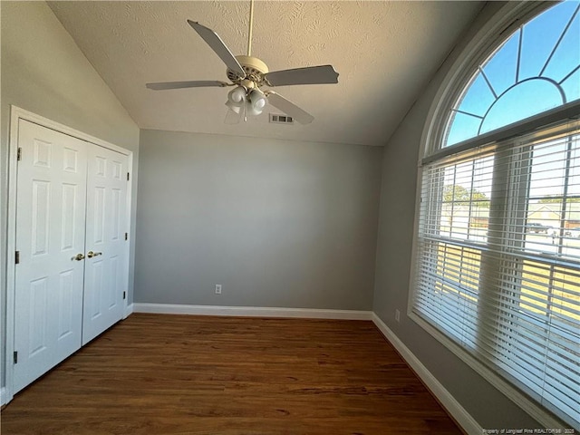 unfurnished bedroom featuring a textured ceiling, lofted ceiling, dark wood-type flooring, a closet, and ceiling fan