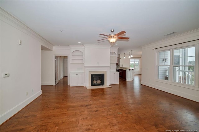 unfurnished living room with ceiling fan, a fireplace with flush hearth, wood finished floors, visible vents, and crown molding