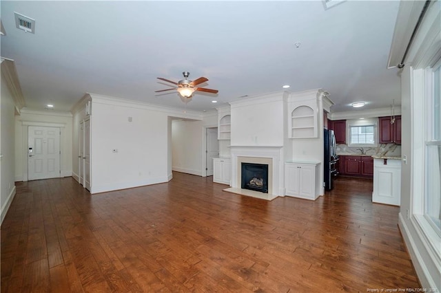 unfurnished living room with a fireplace with flush hearth, ornamental molding, and dark wood finished floors