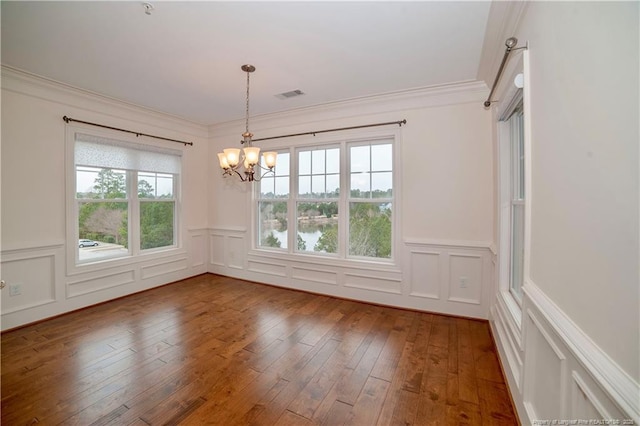 unfurnished dining area featuring visible vents, a decorative wall, hardwood / wood-style floors, and ornamental molding