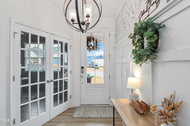 doorway to outside with crown molding, a chandelier, light wood-type flooring, and french doors