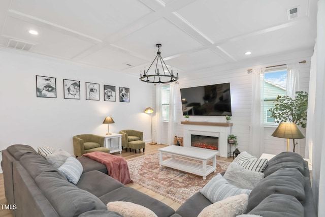 living room with coffered ceiling, a fireplace, wood-type flooring, and a chandelier