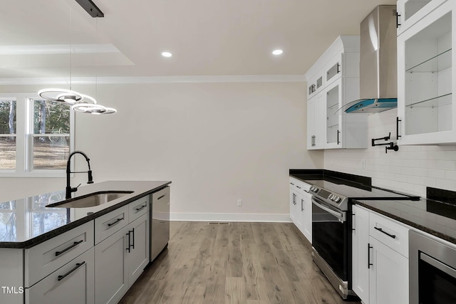 kitchen with pendant lighting, wall chimney range hood, sink, and white cabinets