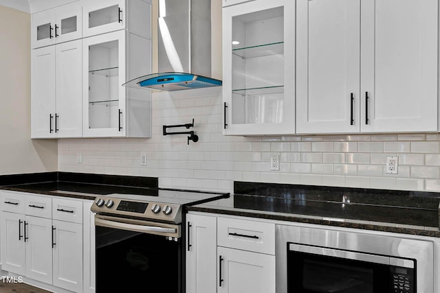 kitchen featuring stainless steel appliances, white cabinetry, wall chimney range hood, and dark stone counters