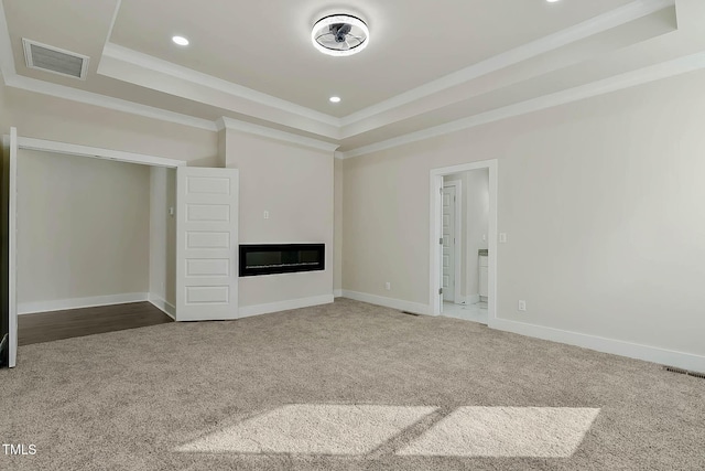 unfurnished living room with a tray ceiling, ornamental molding, and carpet