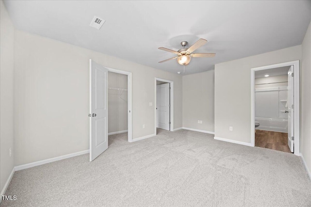 unfurnished bedroom with ceiling fan, ensuite bathroom, a spacious closet, light colored carpet, and a closet