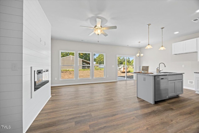 kitchen with sink, a kitchen island with sink, hanging light fixtures, a multi sided fireplace, and stainless steel dishwasher