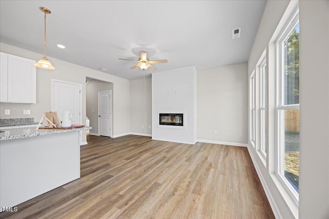 unfurnished living room with ceiling fan, a large fireplace, and wood-type flooring