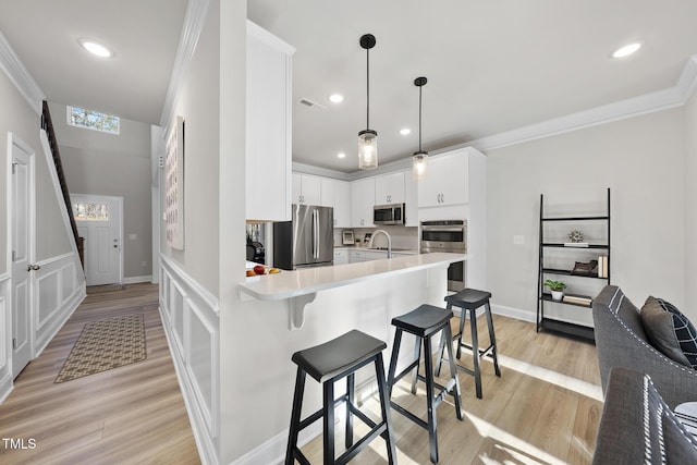 kitchen featuring pendant lighting, white cabinets, a kitchen bar, stainless steel appliances, and light wood-type flooring