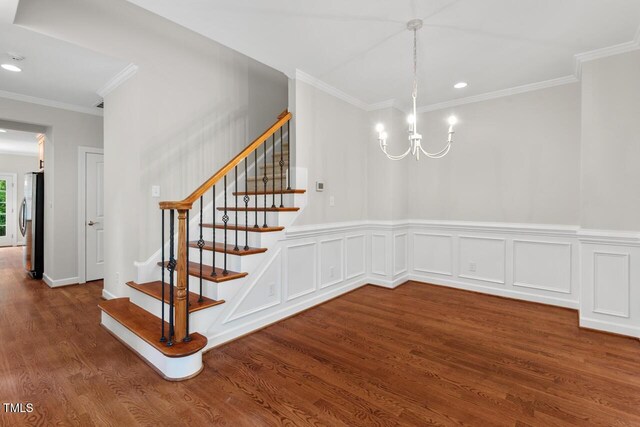 staircase with ornamental molding, recessed lighting, wood finished floors, and a notable chandelier