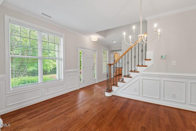 entrance foyer with stairs, a notable chandelier, ornamental molding, and wood finished floors