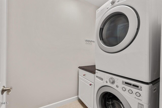 washroom featuring baseboards, cabinet space, light tile patterned flooring, and stacked washer / dryer