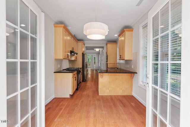 kitchen with gas stove, light brown cabinets, decorative backsplash, light wood-type flooring, and under cabinet range hood