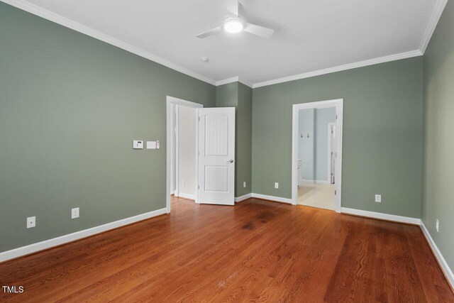 unfurnished bedroom featuring crown molding, baseboards, ensuite bath, and wood finished floors