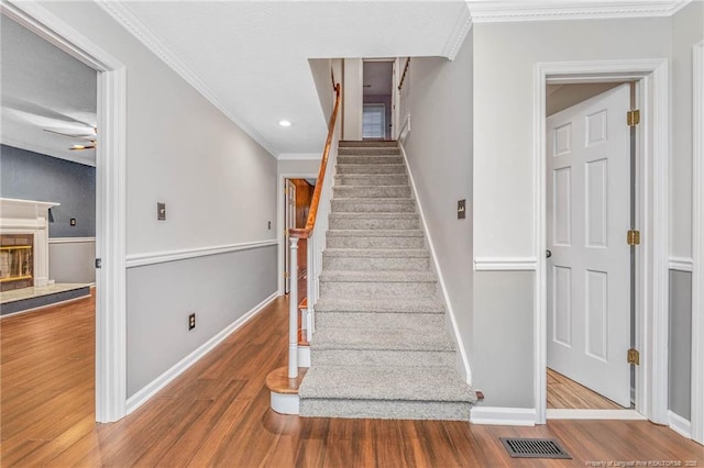 stairway featuring a tile fireplace, crown molding, and hardwood / wood-style floors