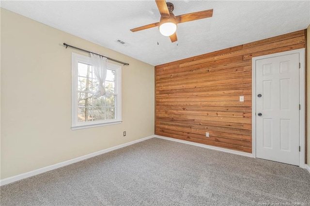 empty room featuring ceiling fan, wood walls, and carpet