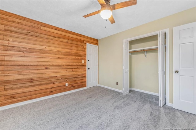 unfurnished bedroom with wood walls, light colored carpet, a closet, and ceiling fan